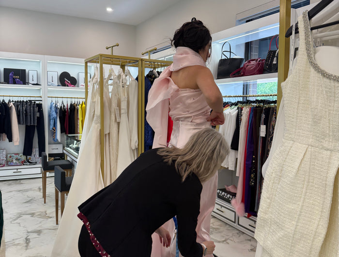 Woman trying on a pink dress at Ellie Belle, a designer fashion, bridal shop and tailoring boutique in Eden Prairie, MN. With a master tailor assisting her.