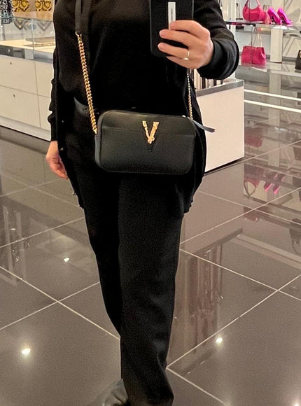 Person wearing Versace black Virtus camera bag crossbody